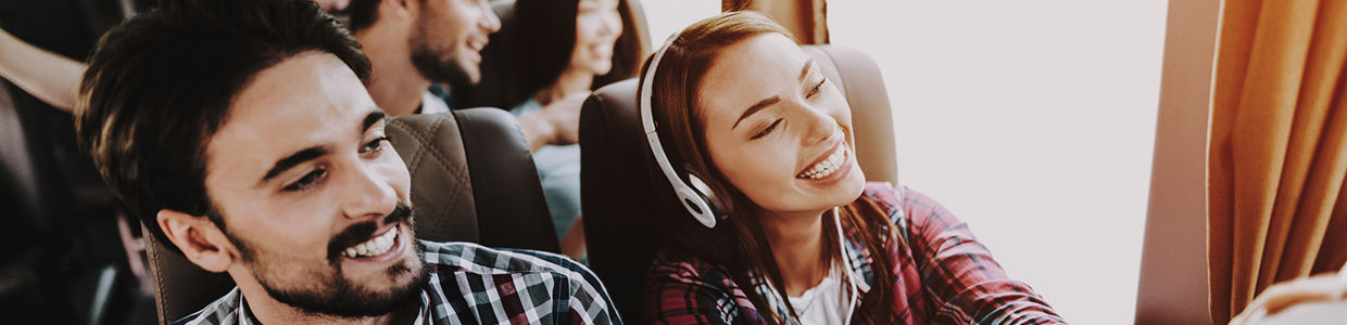 Young Smiling Couple Traveling on Tourist Bus. Handsome Man and Beautiful Woman in Headphones Relaxing on Passenger Seats of Tour Bus. Traveling, Tourism and People Concept. Happy Travelers on Trip